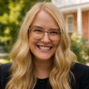 Smiling woman with long blond hair and glasses outdoors.