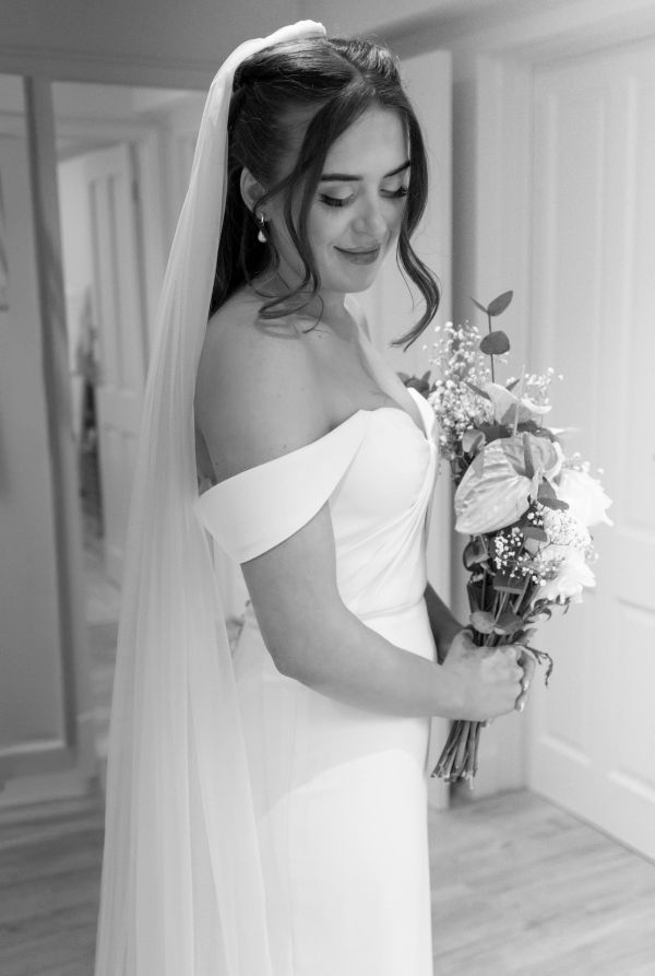 Bride in elegant gown holding bouquet, smiling softly.