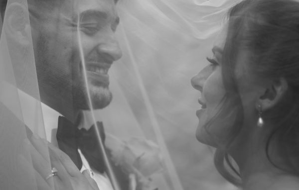 Bride and groom smiling under the wedding veil in a black and white photo.