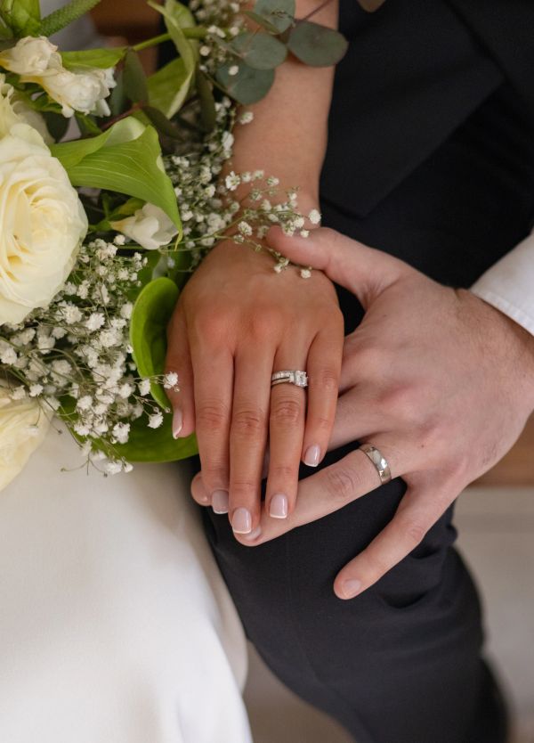 Close-up of a couple's hands with wedding rings and a bouquet.