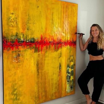 Woman artist posing next to a large yellow and red abstract painting.