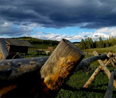Rustic wooden fence in a rural field under a cloudy sky.