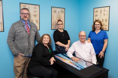 A group of five medical professionals posing in a clinic room with anatomical charts.