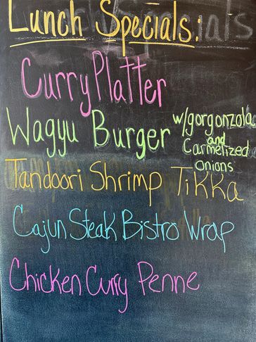 Chalkboard menu with colorful lunch specials including curry, burgers, shrimp, steak wrap, and penne.