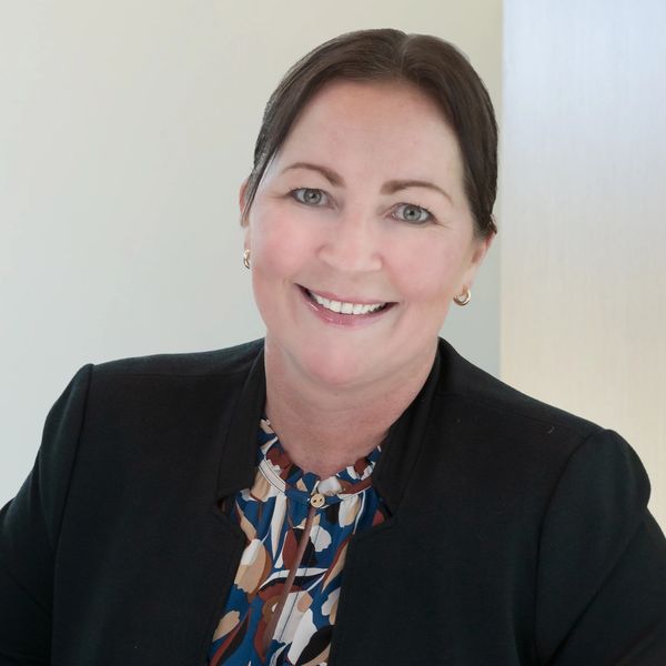 Smiling woman in professional attire with a patterned blouse and black blazer.