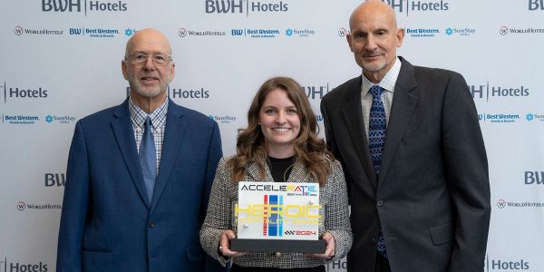 Three people posing with an award at a BWH Hotels event.