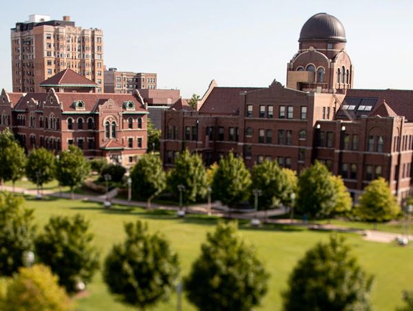 Historic brick building with dome and green park in foreground.