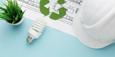 Energy-efficient bulb, hard hat, and recycling symbol on blueprint.