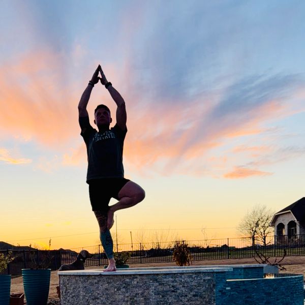 Person practicing yoga at sunset with colorful sky.