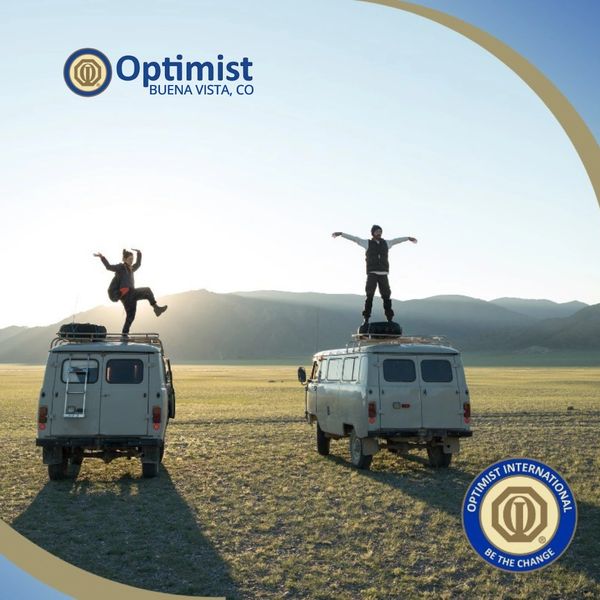 Two people stand joyfully on vans in a vast field at sunrise.