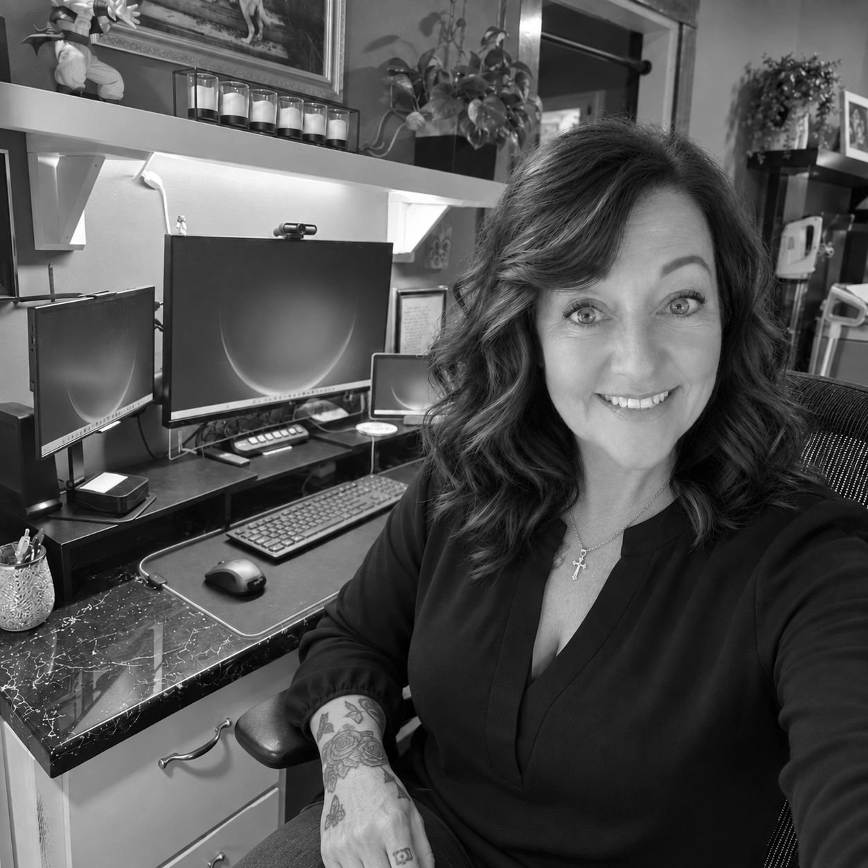Woman smiling at her desk with multiple monitors and tattoos.
