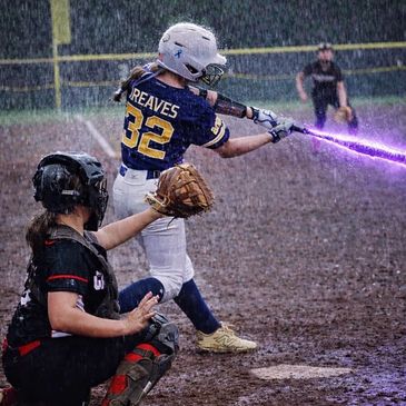 Softball player Reaves hitting a glowing purple bat in the rain.