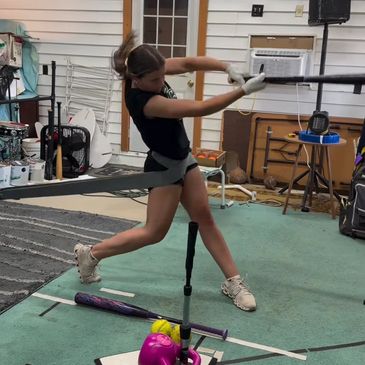Young girl swinging a bat during indoor softball practice.