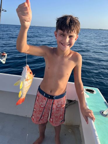 A boy proudly holding a fish on a boat.