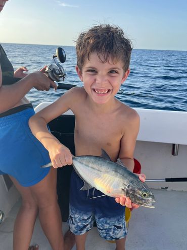 Young boy smiling and holding a fish he caught on a boat.