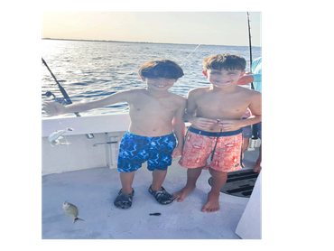 Two boys smiling on a fishing boat with fish caught.
