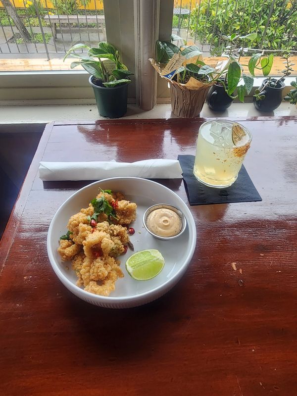 Fried calamari with dipping sauce and a lime wedge, paired with a cocktail on a wooden table.