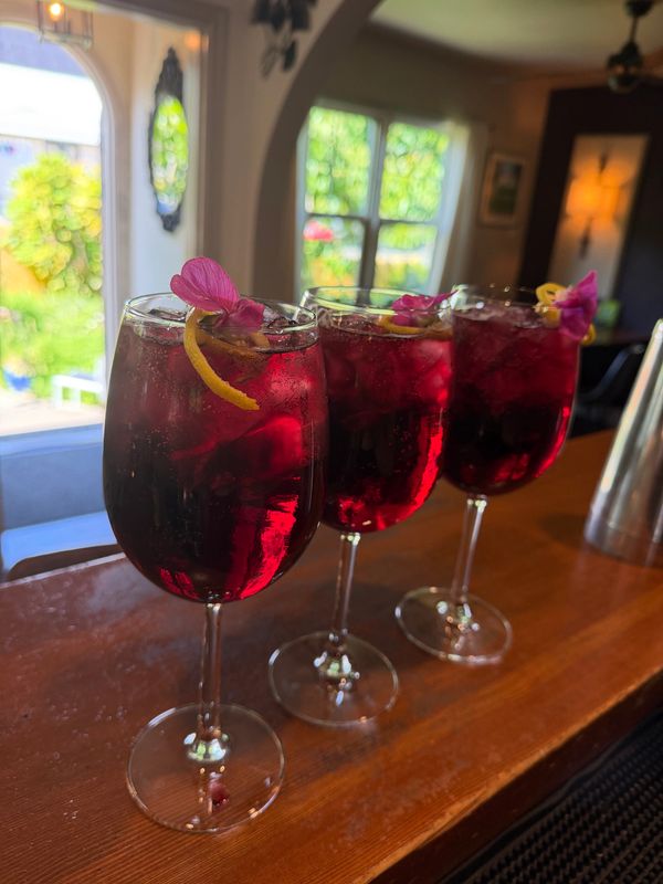 Three elegant red cocktails garnished with lemon twists and pink flowers.
