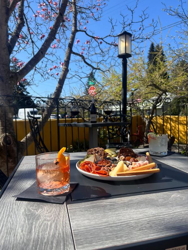 Outdoor table with drinks and a charcuterie plate under blossoming trees.