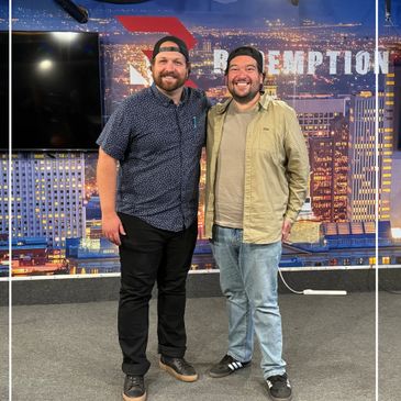 Two smiling men wearing caps pose in front of a cityscape backdrop with the word 'REDEMPTION'.