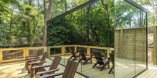 A wooden deck with chairs and a large glass wall reflecting the forest.