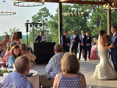 A bride and groom dance at an outdoor wedding reception with guests watching.