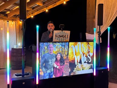 DJ performing at a wedding reception with colorful lights and a photo display.