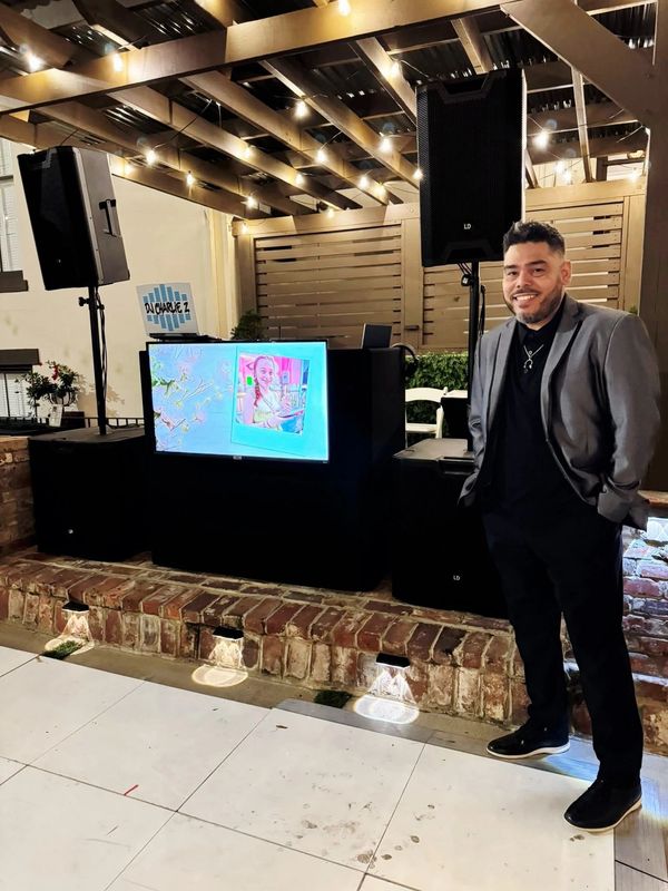 Man in suit standing near DJ setup with lights and screen.