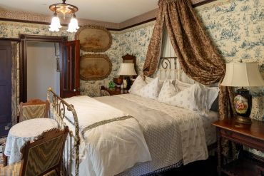 Cozy vintage bedroom with patterned wallpaper and brass bed.