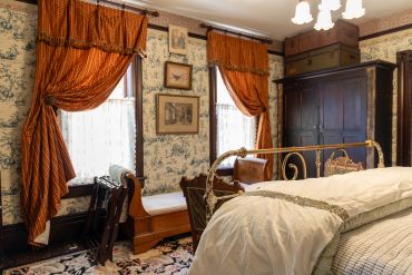 A vintage bedroom with patterned curtains and wooden furniture.