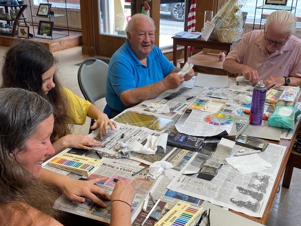 Two women and two men sit around a table working on an art project