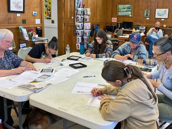 Six women sit around a table and work on an art project
