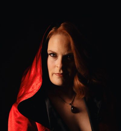 Woman with red hooded cloak against a dark background.