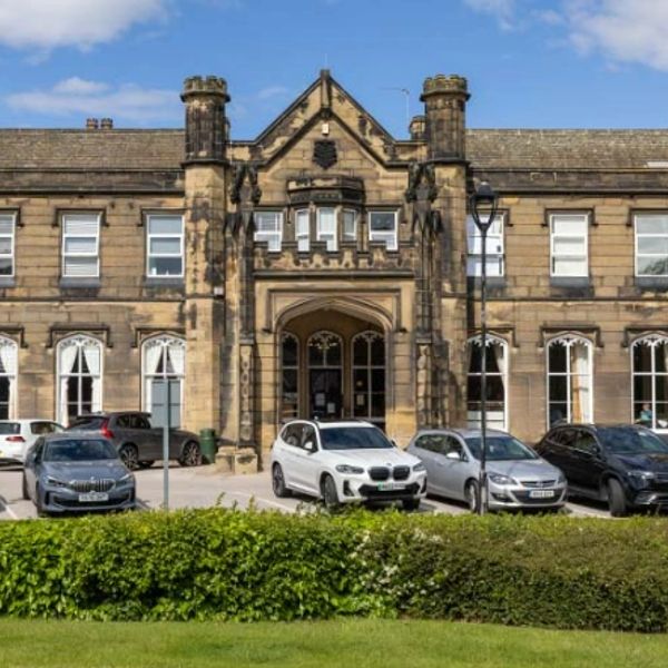 Historic stone building with cars parked in front under blue sky.
