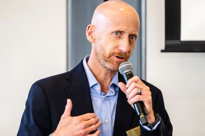 A man in a suit speaking into a microphone during a presentation.