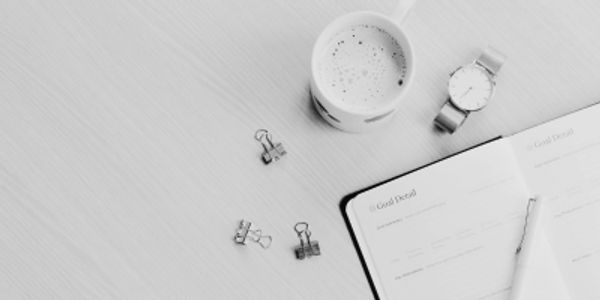 Workspace with a coffee cup, watch, binder clips, and an open planner.