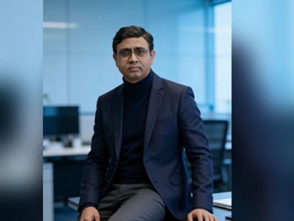 A man in a dark blazer and glasses sitting in a modern office.