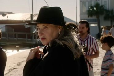 Woman in black hat looking sideways on a sunny beach.