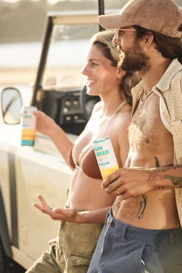 Two friends enjoying drinks outdoors beside a vehicle.