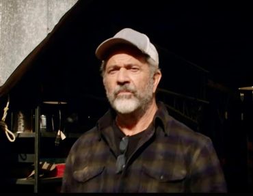 A man with a beard and cap stands outdoors.
