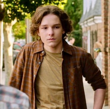Young man with curly hair in a brown shirt looking thoughtful.