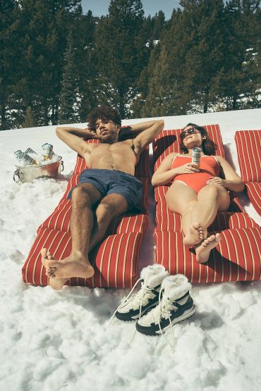 Couple sunbathing on snow in swimwear.