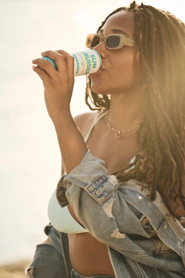 Woman drinking from a can outdoors in sunlight.