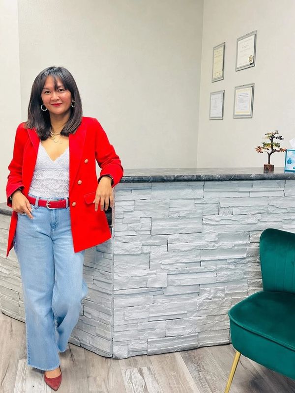 Woman in red blazer and light blue jeans standing by a counter.