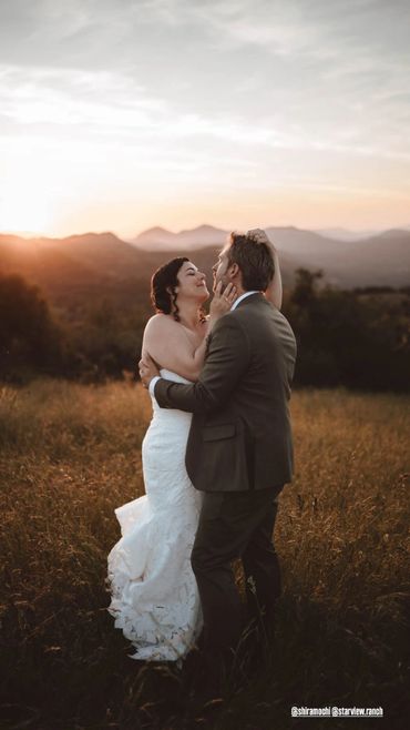 Bride and groom embracing during sunset in a scenic outdoor setting.