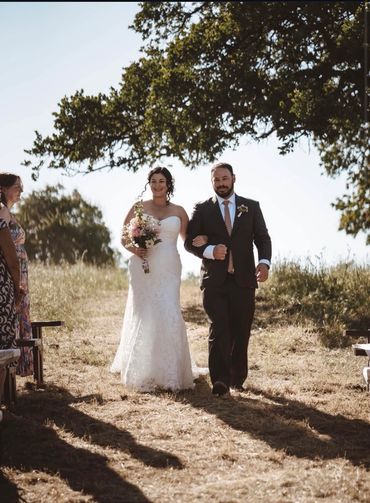 Bride and groom walking arm in arm outdoors under a tree.