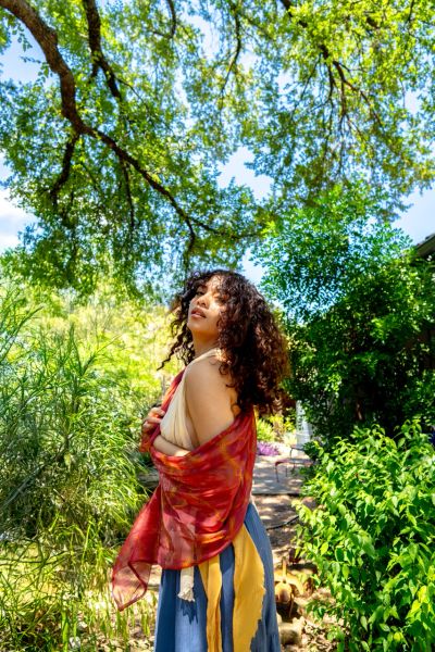 Woman posing outdoors with vibrant shawl in lush greenery.