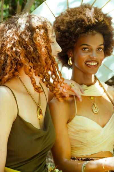 Two women smiling and enjoying a sunny outdoor moment with elegant attire.