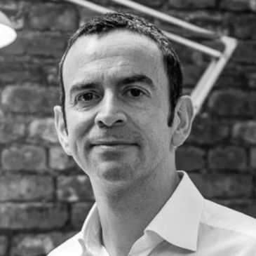 Black and white portrait of a man in a white shirt against a brick wall.