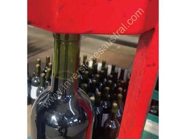 A close-up of a wine bottle being filled on a red bottling machine.